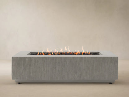 Wilmar Rectangular Natural Gas Fire Pit, gray concrete with textured sides, bright flames over black lava rock. Wooden shingle wall.