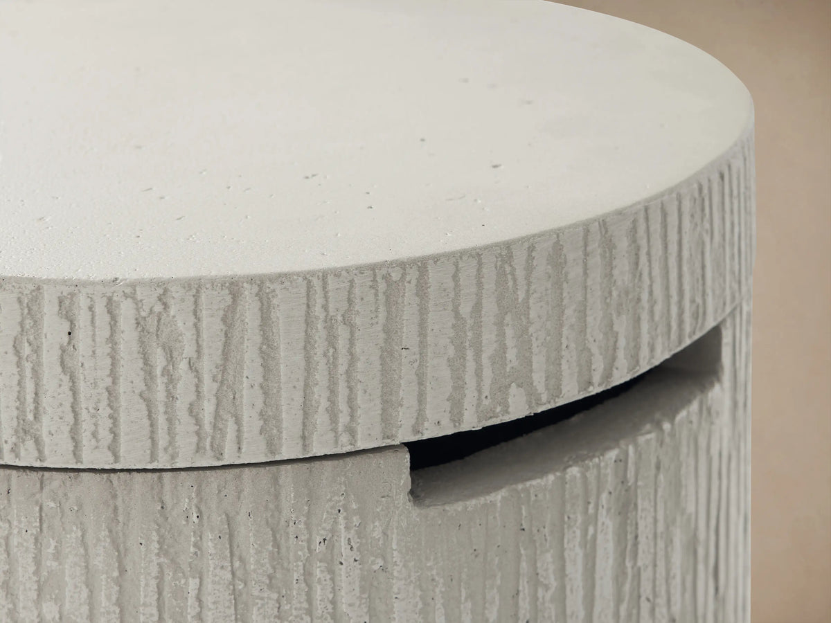 Light gray cylindrical Wilmar Fire Pit Tank Cover with rough, vertically ribbed concrete texture and a dark access slot.
