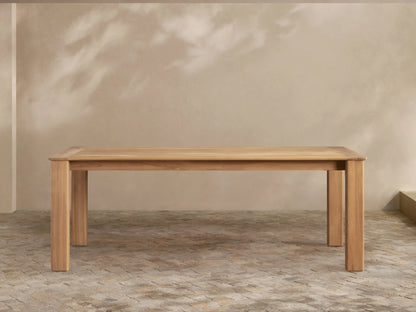 Zoe Outdoor Dining Table: Rectangular, golden-toned natural teak wood with sturdy legs, on a patterned patio floor.