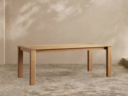 Zoe Outdoor Dining Table: Rectangular, golden-toned natural teak wood with sturdy legs, on a patterned patio floor.