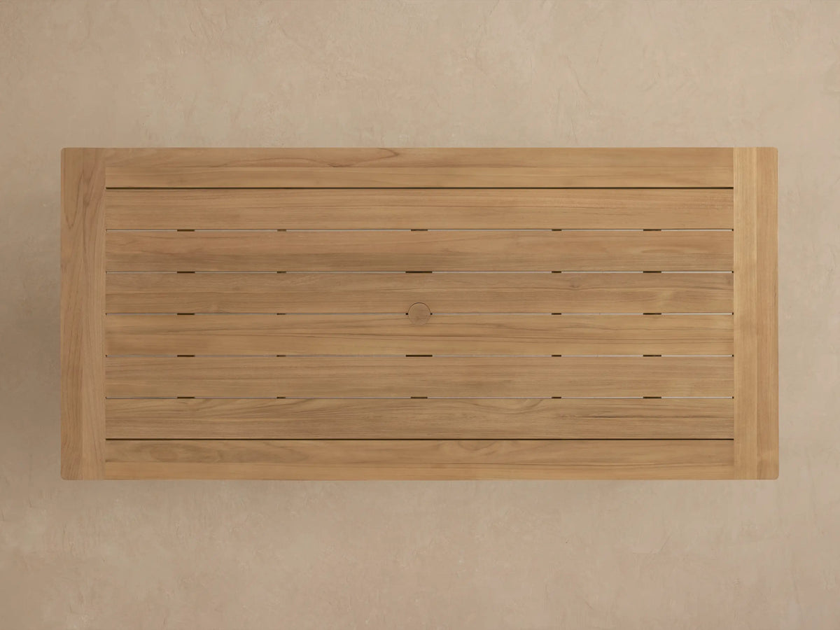 Close-up of Zoe Outdoor Dining Table's natural teak wood top and leg. Light brown planks with visible grain, angled view.