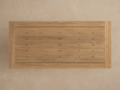 Close-up of Zoe Outdoor Dining Table's natural teak wood top and leg. Light brown planks with visible grain, angled view.