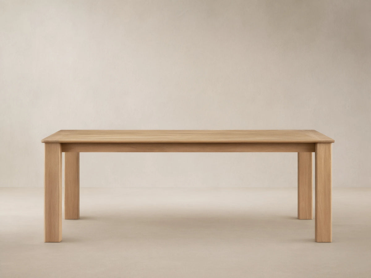 Zoe Outdoor Dining Table: Rectangular, golden-toned natural teak wood with sturdy legs, on a patterned patio floor.