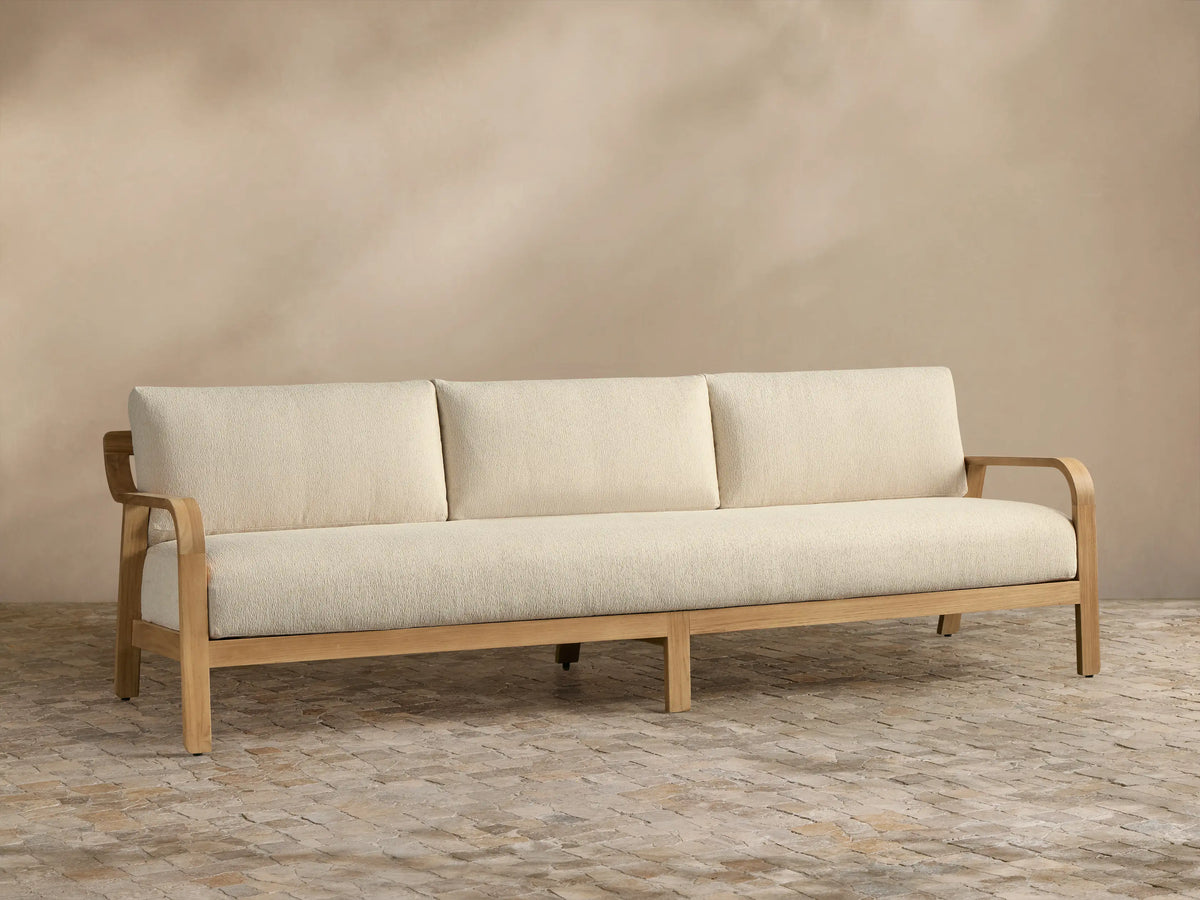 Front view of the Zoe Outdoor Sofa with dark gray cushions, natural teak frame, and patterned throw pillow.