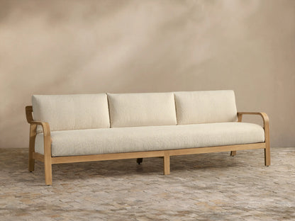 Front view of the Zoe Outdoor Sofa with dark gray cushions, natural teak frame, and patterned throw pillow.