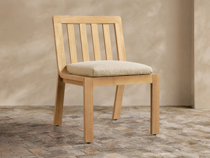 Natural golden teak Zoe Outdoor Dining Side Chair with slatted back, light beige cushion, on tiled floor.