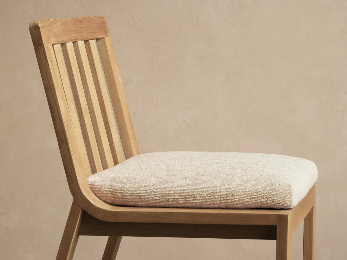 Front view of the Zoe Outdoor Dining Side Chair, crafted from light natural teak wood with a slatted back and light cushion.