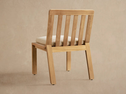 Zoe Outdoor Dining Side Chair, angled. Golden teak wood frame, vertical slatted back, and light cream textured seat cushion.