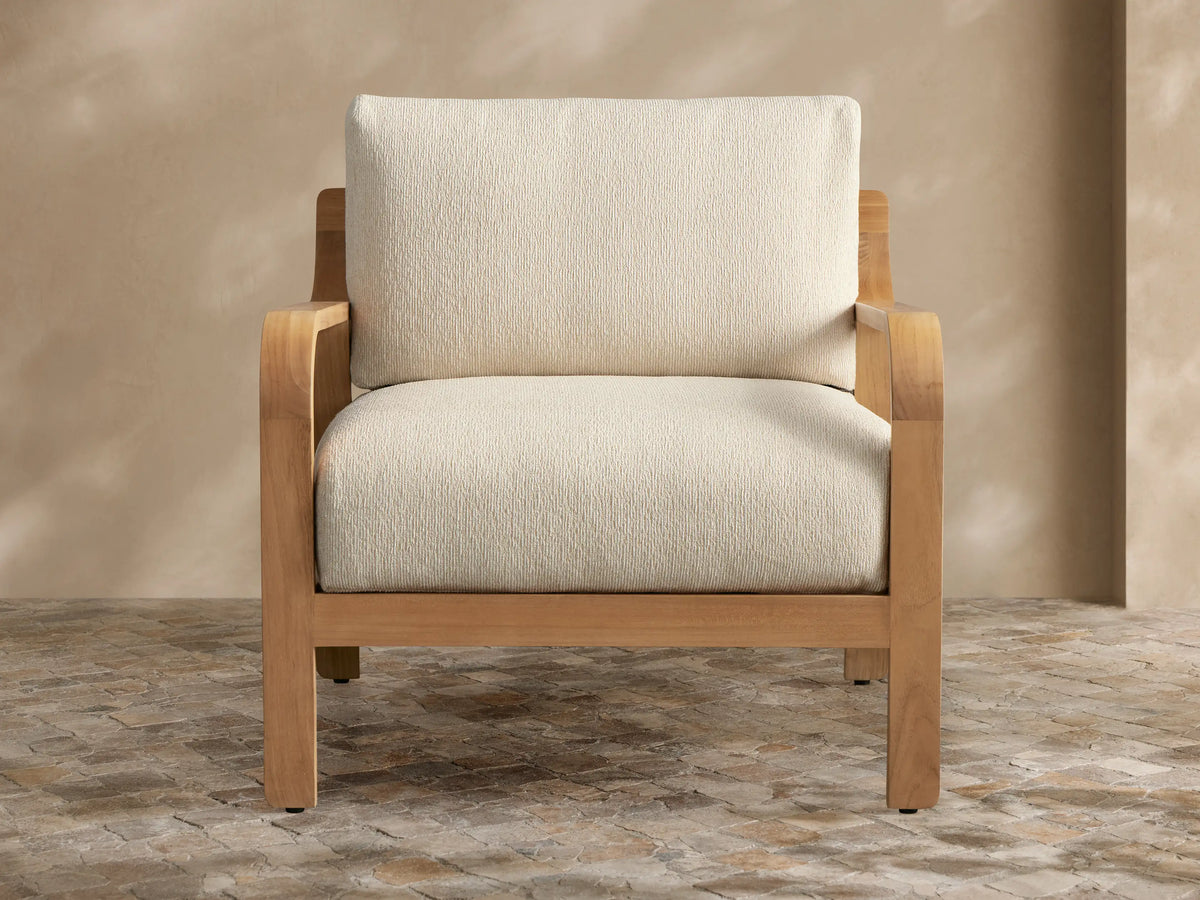 Front-side view of a light striped Zoe Outdoor Lounge Chair, featuring a natural teak frame on a patio.