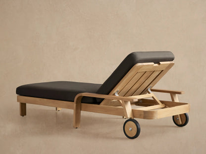 Close-up of a Zoe Outdoor Chaise, light natural teak wood frame with dark gray cushion, showing adjustable back and metal hinge.