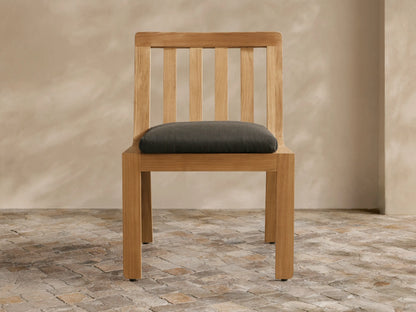Light teak Zoe Outdoor Dining Side Chair with slatted back and dark gray cushion, angled slightly right on a stone floor.