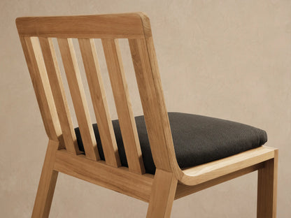 Zoe Outdoor Dining Side Chair, light teak wood with slatted back, dark gray cushion, facing forward on stone tiled floor.
