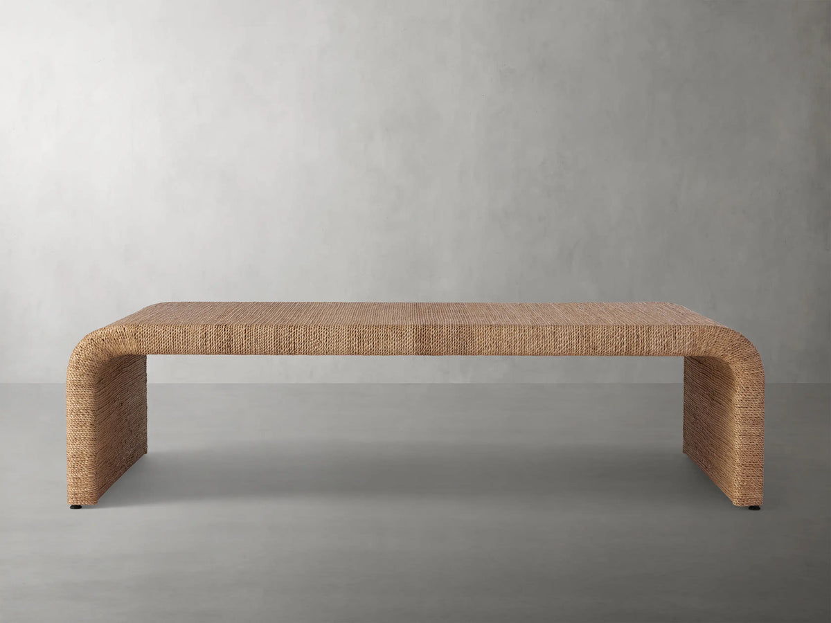 Zoya Sunroom Coffee Table made from woven natural abaca fiber, featuring a sleek rectangular design with curved edges on a gray floor.