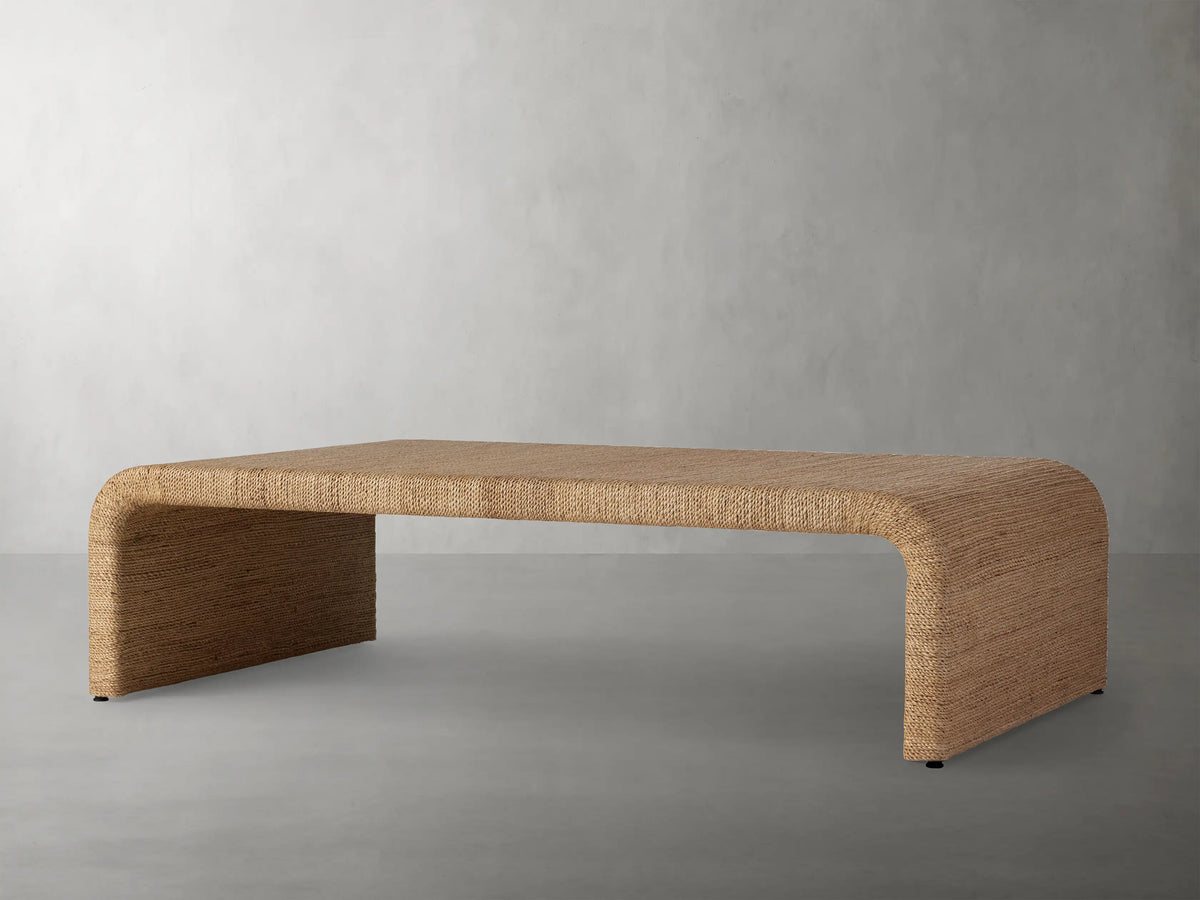 Zoya Sunroom Coffee Table made from woven natural abaca fiber, featuring a sleek rectangular design with curved edges on a gray floor.