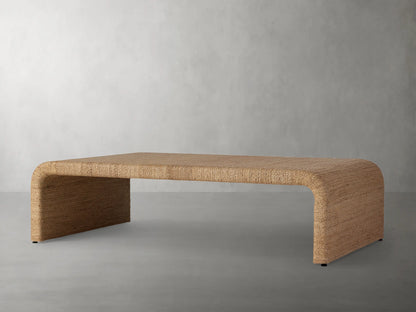 Zoya Sunroom Coffee Table made from woven natural abaca fiber, featuring a sleek rectangular design with curved edges on a gray floor.