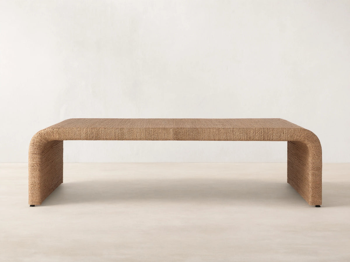 Zoya Sunroom Coffee Table made from woven natural abaca fiber, featuring a sleek rectangular design with curved edges on a gray floor.