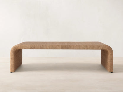 Zoya Sunroom Coffee Table made from woven natural abaca fiber, featuring a sleek rectangular design with curved edges on a gray floor.
