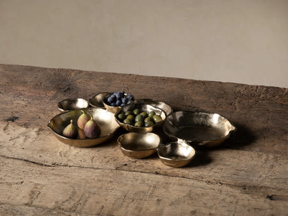 Close-up of multiple dark gold, organically shaped Klasa platters with an antiqued, textured finish on a rustic wooden surface.
