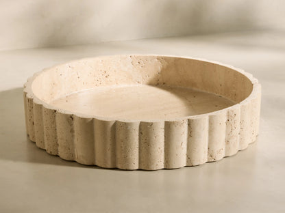 Front view of a beige and ivory-toned Sylvaine Tray, a round porous travertine stone tray with scalloped detailing.