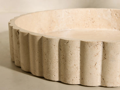 Front view of a beige and ivory-toned Sylvaine Tray, a round porous travertine stone tray with scalloped detailing.