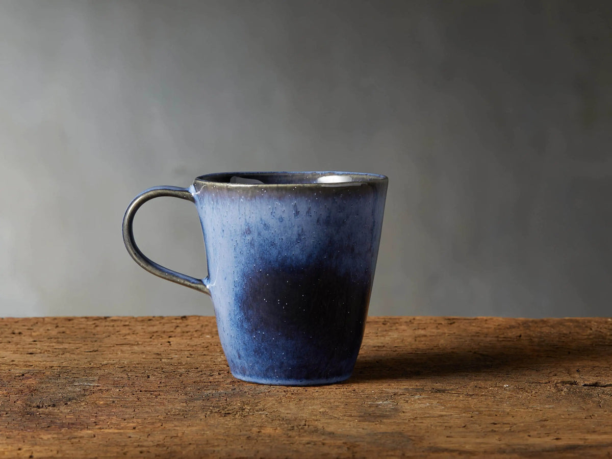 Twilight Mug in deep indigo stoneware with reactive glaze, subtle color variations, curved handle, on wooden surface.