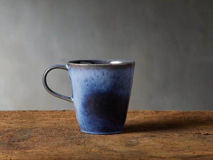 Twilight Mug in deep indigo stoneware with reactive glaze, subtle color variations, curved handle, on wooden surface.