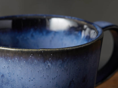 Twilight Mug on a wooden side table next to a matching blue reactive glaze lamp, against a white paneled wall.