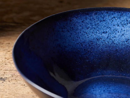Twilight Serving Bowl with rich indigo reactive glaze, handcrafted in stoneware. Blue interior with slight color variance, set on wooden surface.