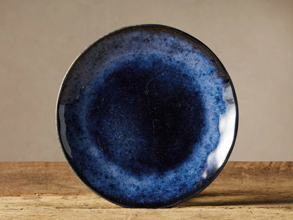 Twilight Salad Plate: round, deep indigo blue stoneware plate with reactive glaze, dark center, lighter blue outer band, on wood.