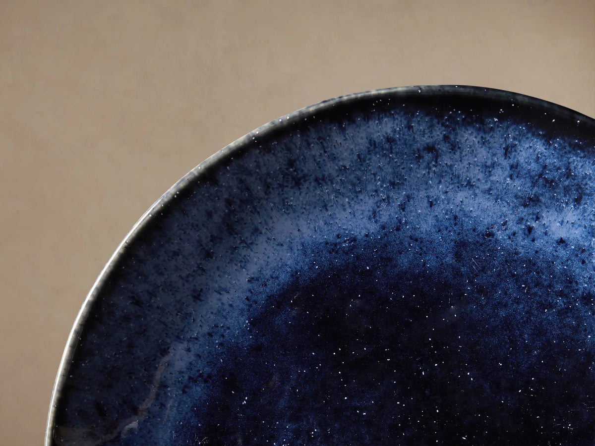 Twilight Salad Plate: round, deep indigo blue stoneware plate with reactive glaze, dark center, lighter blue outer band, on wood.