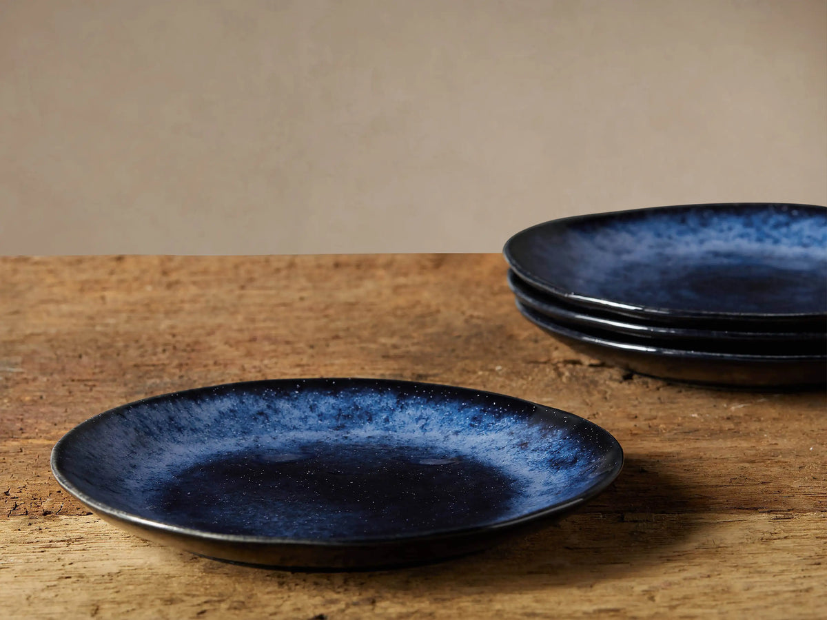 Close-up of a Twilight Salad Plate, showcasing its indigo reactive glaze with lighter specks, like a starry night. Beige background.