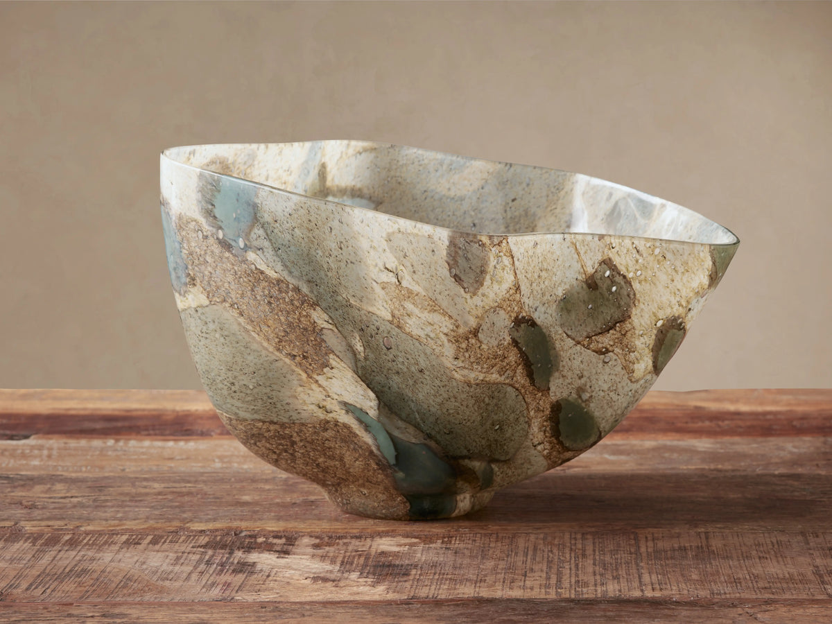 Andromeda Organic Bowl, mouth-blown glass with organic shape, swirling earthy blue, green, brown, and gray patterns on wood.
