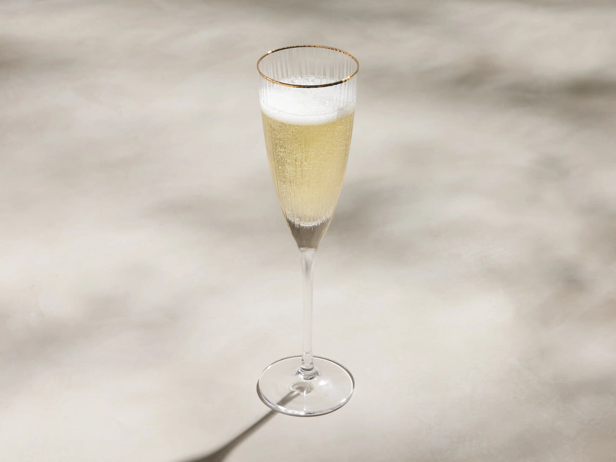 Anisa Champagne Glass, clear ribbed flute with a hand-painted gold rim, standing upright against a light background.