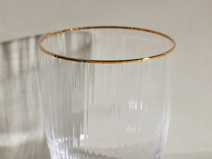 Four clear, ribbed Anisa Double Old Fashioned Glasses with gold rims. One contains an amber drink with ice and orange peel.