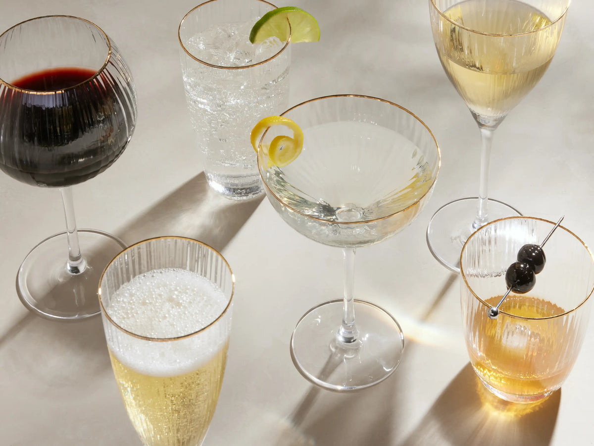 Two clear, ribbed Anisa Double Old Fashioned glasses with gold rims, filled with drinks, one with ice, the other a lemon slice.