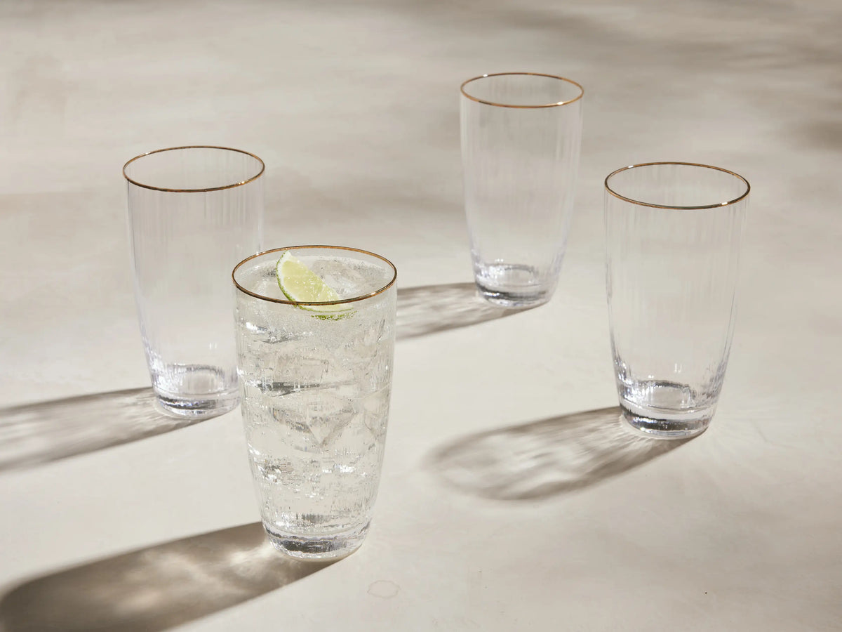 Set of 4 Anisa highball glasses: clear ribbed glass with gold rims. One has ice, liquid & lime; 3 are empty.