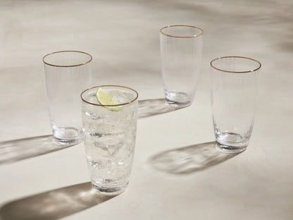 Set of 4 Anisa highball glasses: clear ribbed glass with gold rims. One has ice, liquid & lime; 3 are empty.