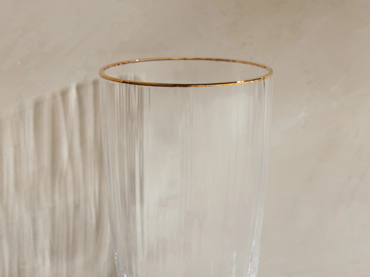 Set of 4 Anisa highball glasses: clear ribbed glass with gold rims. One has ice, liquid & lime; 3 are empty.