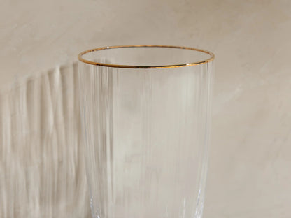 Set of 4 Anisa highball glasses: clear ribbed glass with gold rims. One has ice, liquid & lime; 3 are empty.