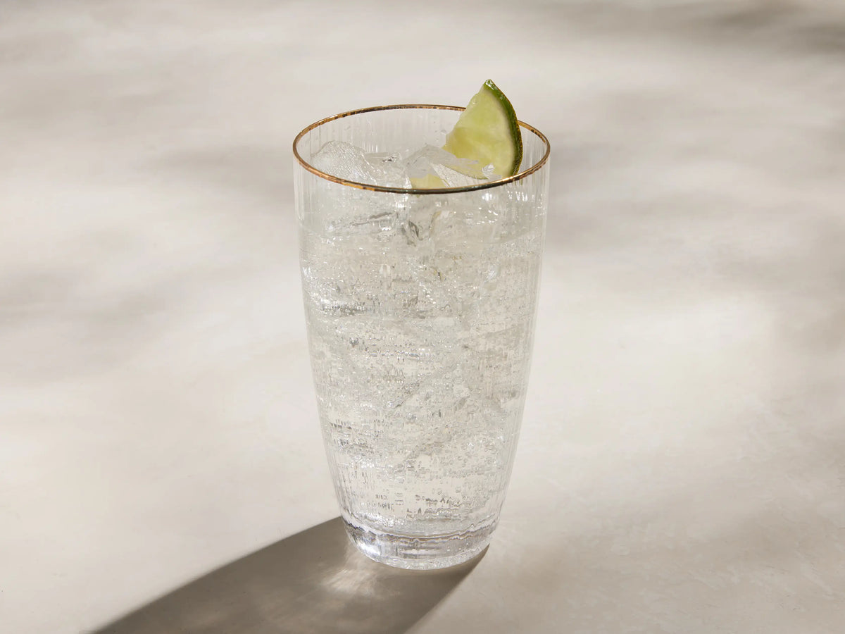 Anisa highball glass: close-up of a clear, ribbed glass with a thin gold rim against a light background.