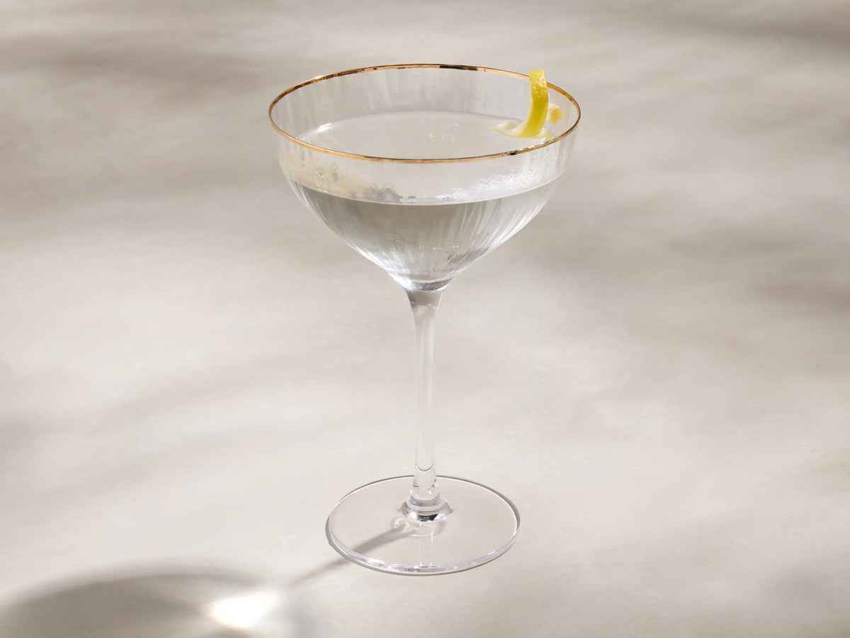 Clear Anisa cocktail glass with a hand-painted gold rim and ribbed texture on the bowl, angled against a light background.