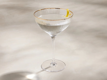 Clear Anisa cocktail glass with a hand-painted gold rim and ribbed texture on the bowl, angled against a light background.