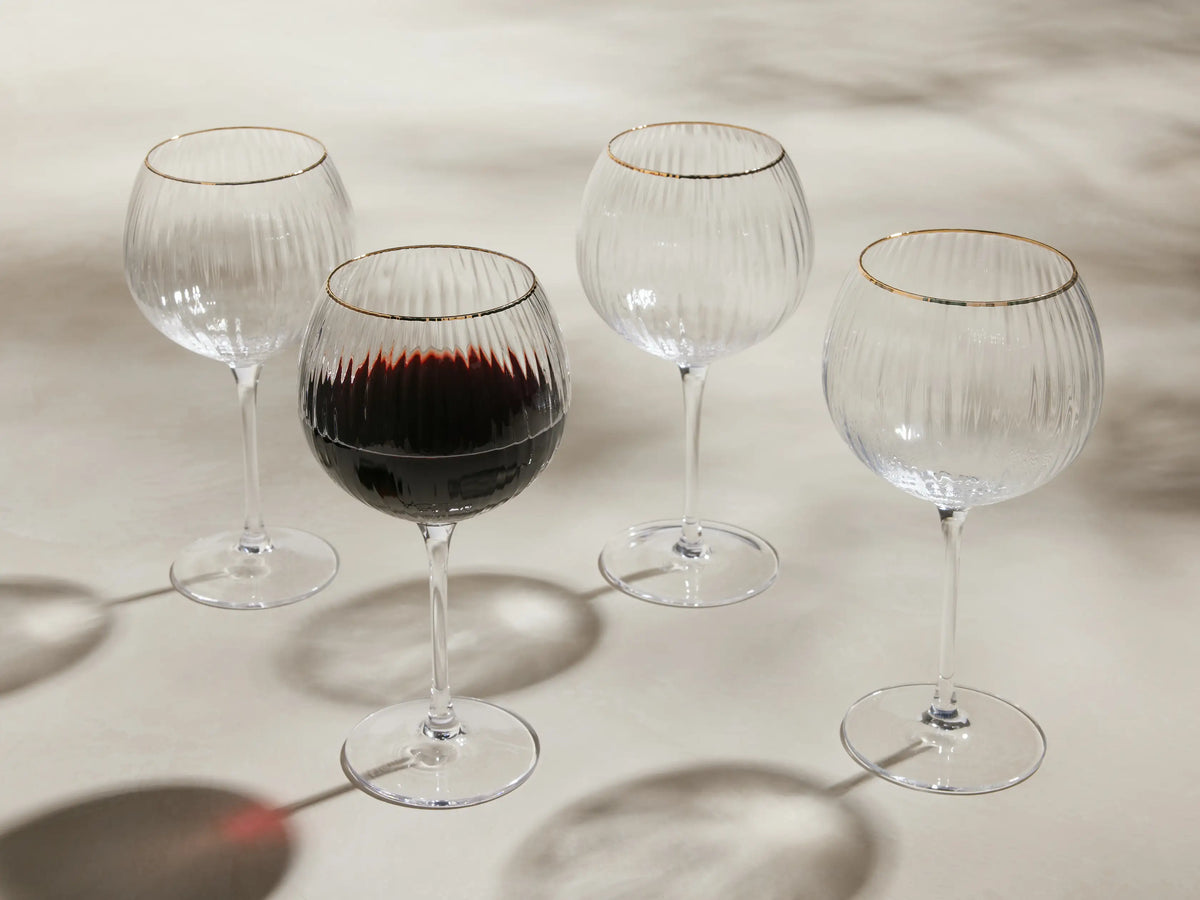 Front view of four clear Anisa Red Wine Glasses with ribbed bowls and gold rims, one filled with red wine.