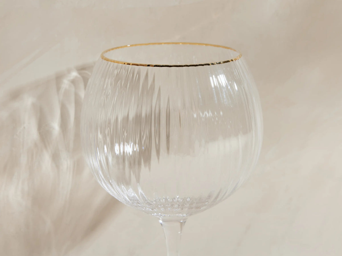 Front view of four clear Anisa Red Wine Glasses with ribbed bowls and gold rims, one filled with red wine.