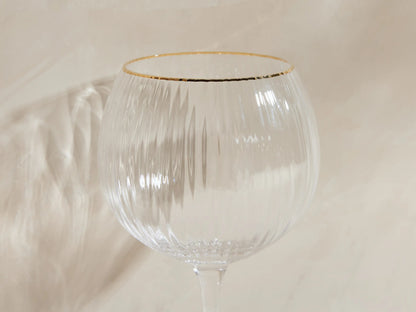 Front view of four clear Anisa Red Wine Glasses with ribbed bowls and gold rims, one filled with red wine.