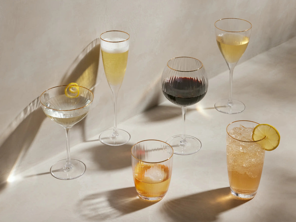 Front view of Anisa Red Wine Glasses, clear ribbed glass with a gold rim, filled with dark red wine.