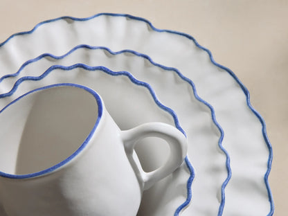 Capuchos Dinnerware: White matte ruffled plate, cereal bowl, mug on plate, all with blue hand-painted rims.