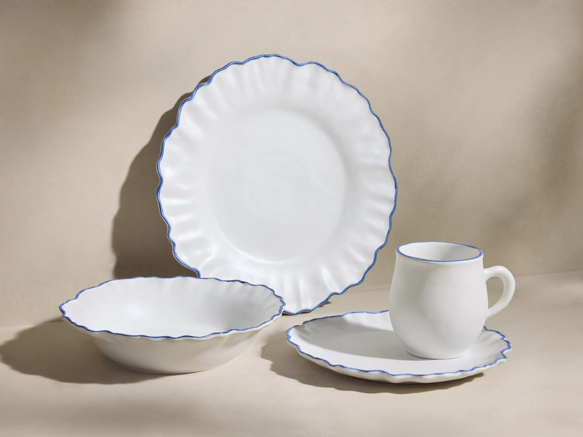 Capuchos Dinnerware: white matte large plate, pasta bowl, mug, and salad plate, all with blue ruffled edges.