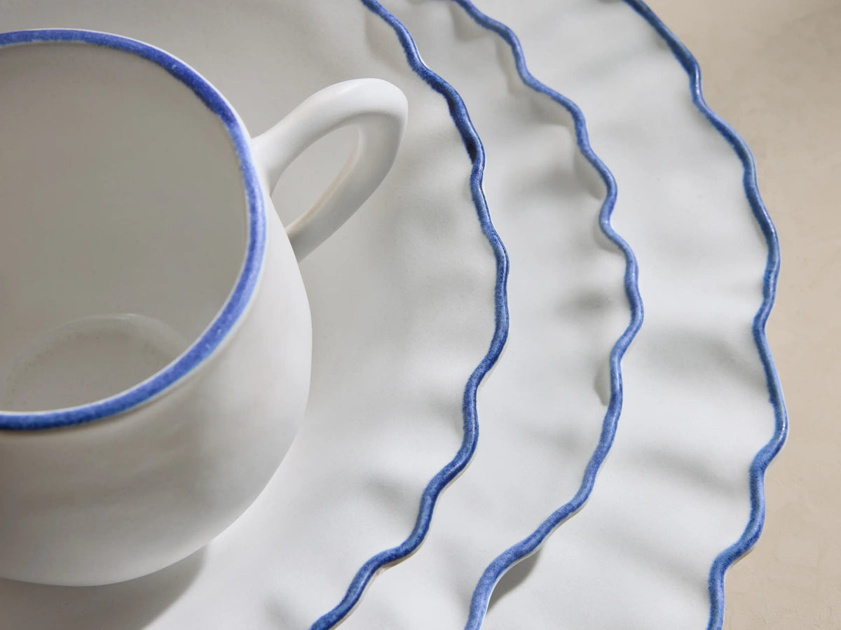 Capuchos Dinnerware: white matte large plate, pasta bowl, mug, and salad plate, all with blue ruffled edges.