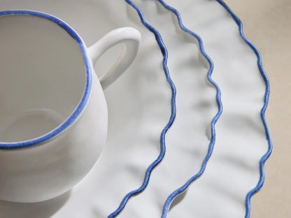 Capuchos Dinnerware: white matte large plate, pasta bowl, mug, and salad plate, all with blue ruffled edges.